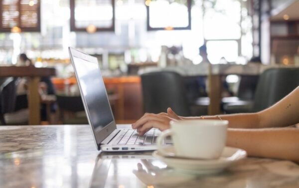 Hands working at a laptop with a cup of coffee