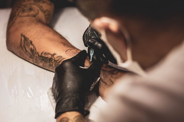 A tattoo artist tattooing somebodies arm.