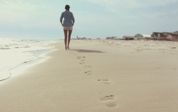 A woman walks along a shoreline leaving footprints in the sand