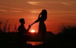 Silhouette of a couple during a marriage proposal at sunset, capturing a romantic moment with warm hues in the background.
