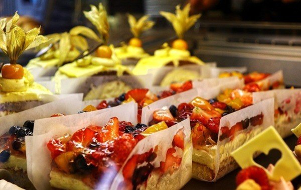 An assortment of colorful fruit-topped pastries displayed for food delivery and takeout, featuring layers of cream, sponge cake, and vibrant berries.