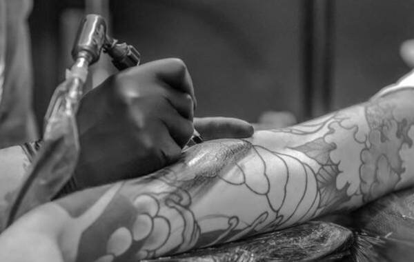 Tattoo artist meticulously inking intricate designs on a client's arm, showcasing the artistry and craftsmanship of tattoo culture.