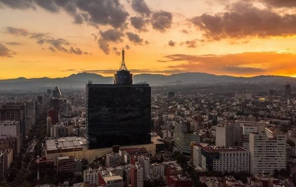 A breathtaking sunset over Mexico City, showcasing a panoramic view of urban architecture, with the prominent Torre Latinoamericana silhouetted against vibrant orange and yellow skies.