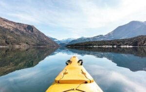 Kayaking on a serene lake in New Zealand, surrounded by majestic mountains and reflective waters under a clear blue sky.