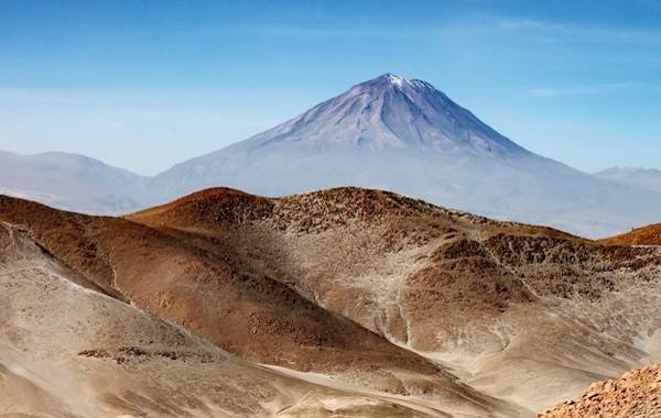 Stunning landscape featuring the snow-capped volcano, Misti, rising majestically above arid hills in Peru, under a clear blue sky.