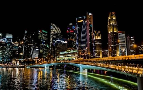 Night view of Singapore's skyline featuring illuminated skyscrapers and a city bridge reflecting in the water.