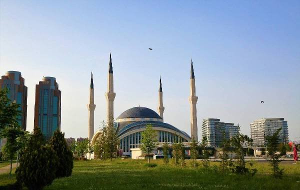 Modern skyline of Ankara, Turkey, featuring a prominent mosque with tall minarets surrounded by greenery and contemporary buildings.