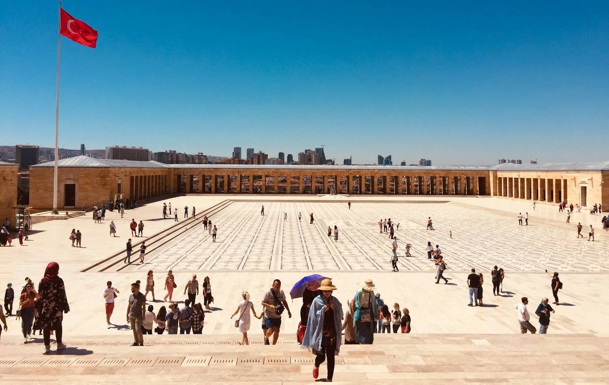 Crowds explore the iconic Anıtkabir, the mausoleum of Mustafa Kemal Atatürk, in Ankara, Turkey, with the Turkish flag flying in the background against a clear blue sky.