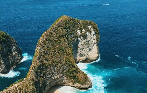 Aerial view of Kelingking Beach in Nusa Penida, Bali, Indonesia featuring a unique cliff formation jutting into the blue ocean.