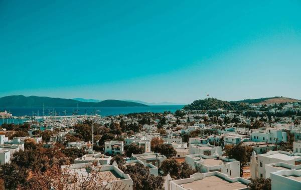 Panoramic view of Bodrum, Turkey, showcasing whitewashed buildings, lush greenery, and a serene harbor against a clear blue sky.