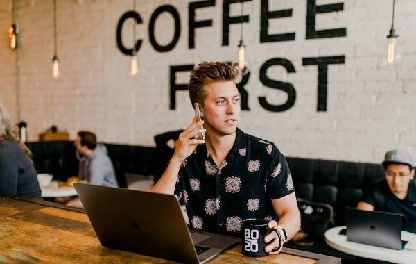 Digital nomad working in a trendy coffee shop on a laptop while talking on the phone