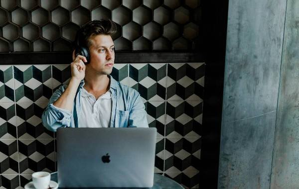 Young digital nomad working on a laptop with headphones in a modern cafe setting.