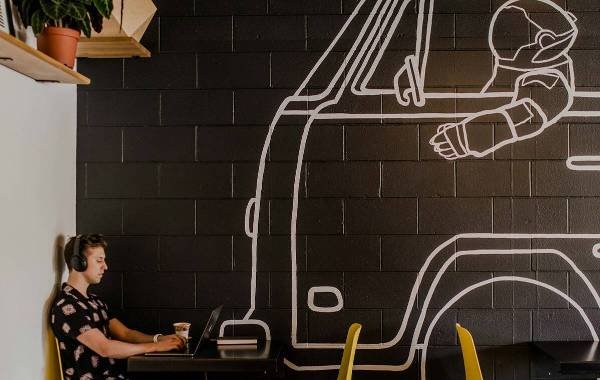 Digital nomad working on laptop in trendy cafe with space-themed wall art