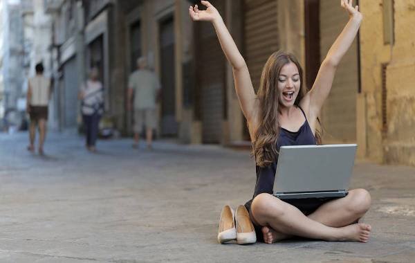 Young woman celebrating while working on a laptop in a city street, representing digital nomad lifestyle