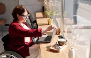 Woman in a wheelchair working on a laptop in a cafe near a window