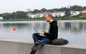 Digital nomad working on laptop by a lakeside in a serene urban environment