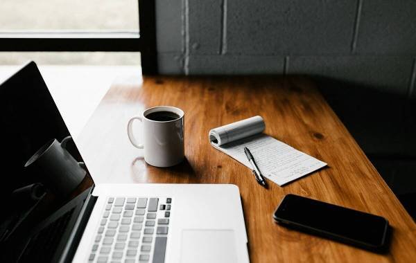 Workspace of a digital nomad with a laptop, coffee cup, notepad, pen, and smartphone on a wooden desk.