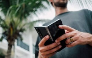 Digital nomad working on a foldable smartphone outdoors with palm trees in the background