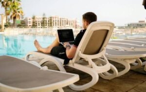 Man working on laptop by hotel swimming pool with cityscape in background - digital nomad lifestyle.