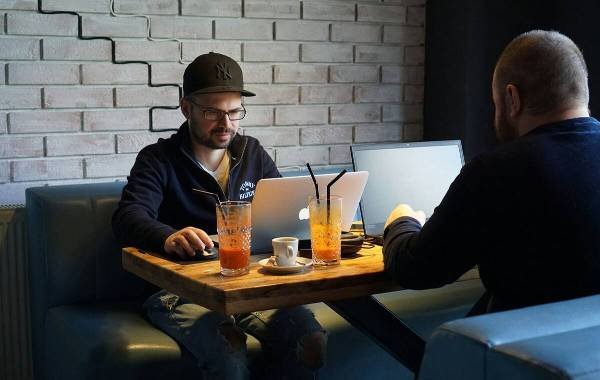 Two digital nomads working on laptops in a modern cafe, with drinks on the table