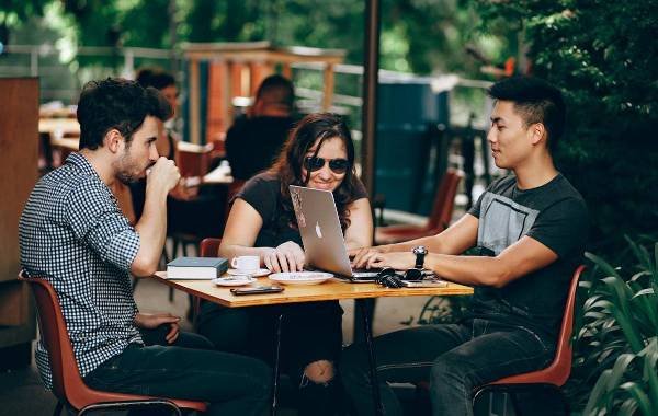 Three digital nomads working together at an outdoor cafe with laptops and coffee.