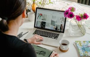 Woman working remotely on a laptop at a bright, creative workspace adorned with flowers and art supplies.