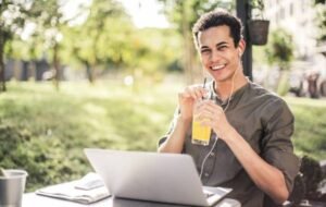 Young man working on a laptop outdoors, enjoying a beverage, representing the digital nomad lifestyle.