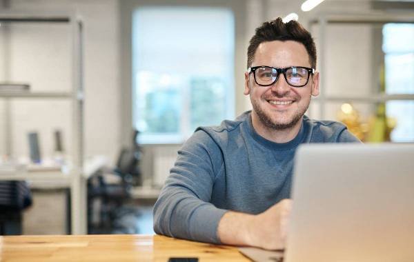 Man working on laptop in shared office space, smiling at camera