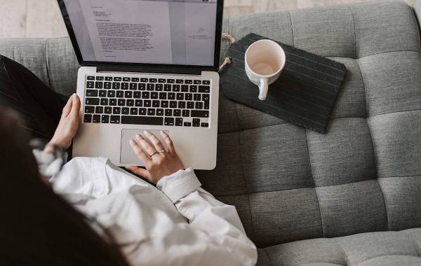 Person working on a laptop with a cup of coffee on a cushioned sofa, illustrating the digital nomad lifestyle.