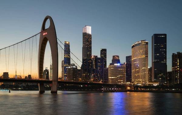 Cityscape of Guangzhou, China at dusk featuring the iconic Canton Tower and modern skyscrapers reflecting on the water.