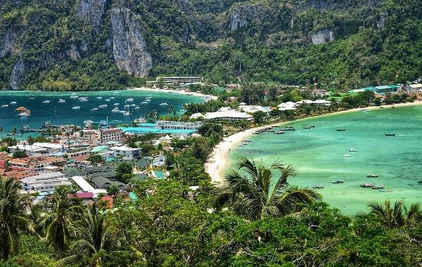 Scenic view of Krabi, Thailand featuring turquoise waters, lush green hills, a vibrant town, and boats in the bay.