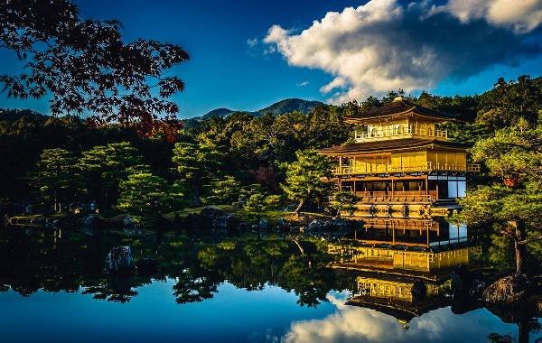 A temple over looking a lake with lush green trees surrounding with a cloud overhead