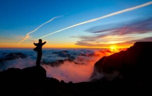 man standing over the ledge and looking over the sunset