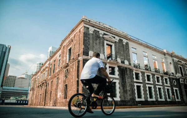 A cyclist rides past a historic building in Manila, Philippines, showcasing colonial architecture amidst a modern cityscape.