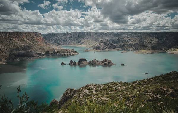 Scenic view of a turquoise lake surrounded by rugged mountains and dramatic clouds in Mendoza, Argentina.