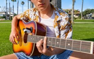 Person playing an acoustic guitar outdoors with an Insta360 GO 3 camera mounted on the instrument