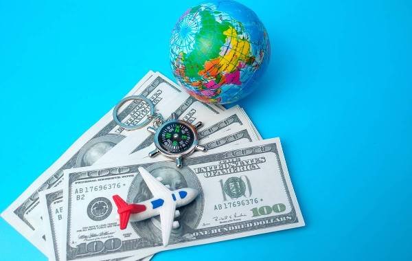 Toy plane on dollar bills next to a globe and compass on blue background, representing travel costs.