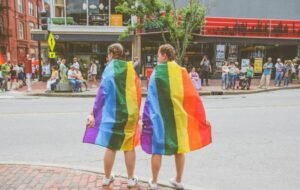 Two people wrapped in rainbow flags standing on a street during an LGBT pride event.
