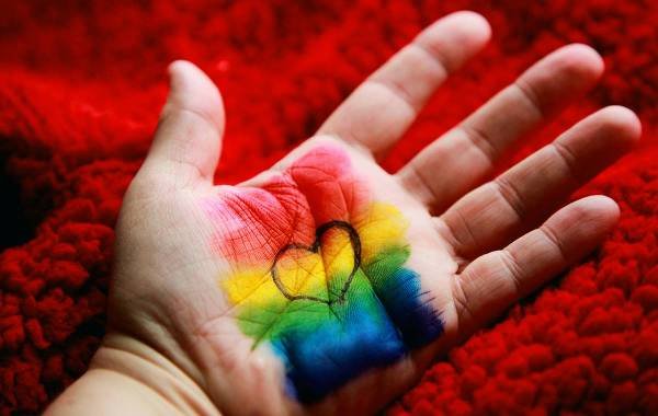 Hand with rainbow colors and heart symbol on red background celebrating LGBT pride.