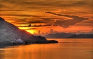 Stunning sunset over Komodo Island, showcasing vibrant orange and yellow hues reflecting on calm waters, with silhouetted mountains in the background. Perfect for nature lovers and travel enthusiasts.