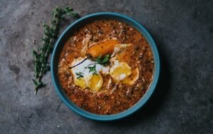 Bowl of traditional Colombian soup featuring tender shredded meat, two poached eggs, and a slice of carrot, garnished with fresh herbs