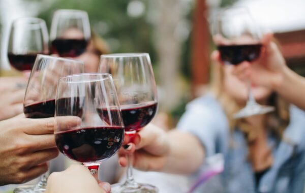 A group of friends clinking glasses of red wine in a lively outdoor setting, celebrating food and wine together