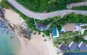 Aerial view of a tropical beachfront property in Koh-Lanta featuring palm trees, sandy beaches, and a serene swimming pool