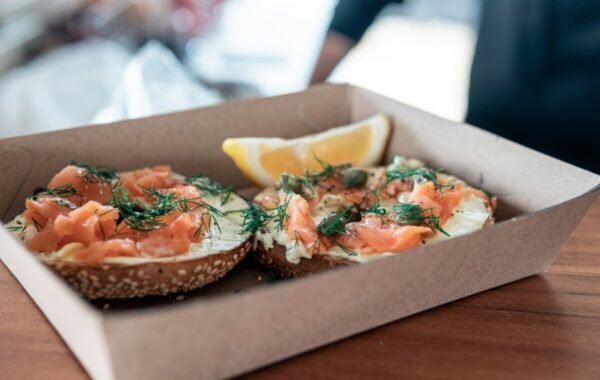 Delicious smoked salmon bagels served in a takeout container, garnished with dill and accompanied by a lemon wedge, perfect for food delivery