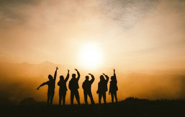 Silhouette of a group of friends joyfully raising their arms against a stunning sunset backdrop, capturing the essence of travel and camaraderie