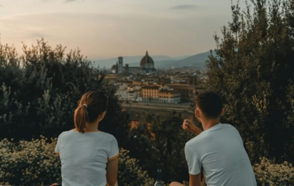 Two friends enjoying a scenic view of Florence at sunset, sitting among greenery