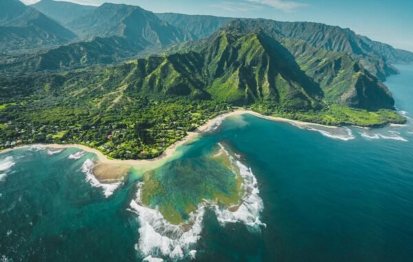 Aerial view of Hawaii's lush mountains and coastline, showcasing vibrant green landscapes meeting crystal-clear waters and sandy beaches