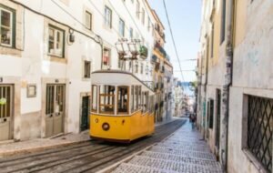 Colorful yellow tram navigating the steep streets of Lisbon, surrounded by charming white buildings and cobblestone pathways