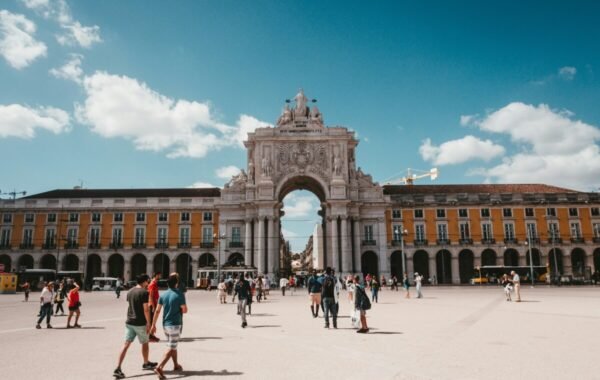 People walking in the Praça do Comércio square in Lisbon, featuring the iconic Arco da Rua Augusta and historic yellow buildings under a bright blue sky