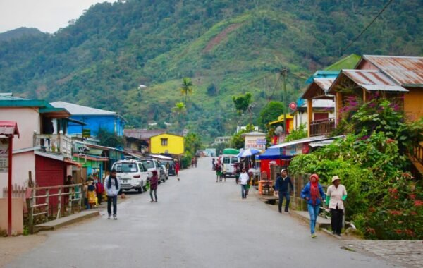 Colorful street scene in Madagascar featuring local shops and villagers, with lush hills in the background